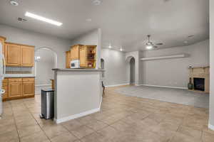 Kitchen with a tile fireplace, tasteful backsplash, light tile patterned floors, ceiling fan, and light brown cabinets