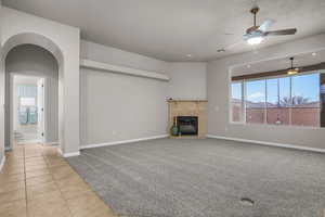 Unfurnished living room featuring light tile patterned flooring, a textured ceiling, ceiling fan, and a fireplace