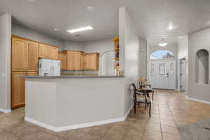 Kitchen featuring white fridge with ice dispenser, light brown cabinets, light tile patterned floors, and kitchen peninsula