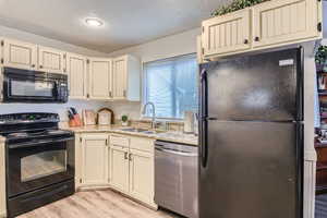 Kitchen featuring sink, black appliances, a textured ceiling, light hardwood / wood-style floors, and cream cabinetry