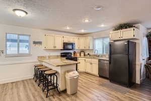 Kitchen featuring a breakfast bar, black appliances, sink, kitchen peninsula, and light stone countertops