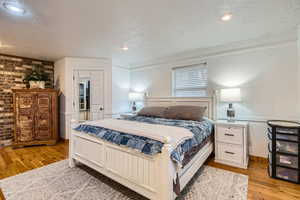 Bedroom with a textured ceiling, brick wall, and light wood-type flooring