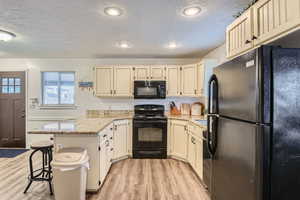 Kitchen with a breakfast bar, light wood-type flooring, kitchen peninsula, light stone countertops, and black appliances