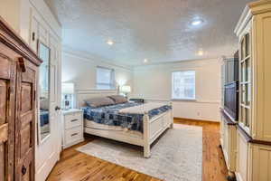 Bedroom with light hardwood / wood-style floors, multiple windows, and a textured ceiling