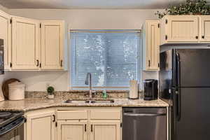 Kitchen featuring dishwasher, black fridge, sink, and light stone counters