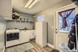 Clothes washing area with sink, washing machine and dryer, cabinets, a textured ceiling, and light hardwood / wood-style floors