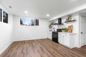 Bar featuring sink, white cabinetry, black range with gas stovetop, dark hardwood / wood-style flooring, and wall chimney range hood