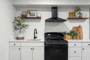 Kitchen with wall chimney exhaust hood, black gas stove, sink, and white cabinets