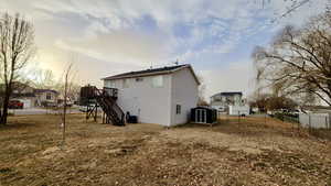 Back house at dusk featuring a wooden deck, a yard, and cooling unit