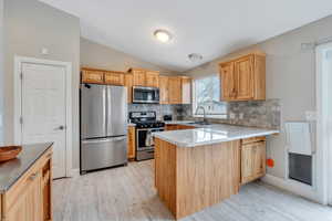 Kitchen featuring light brown cabinetry, vaulted ceiling, kitchen peninsula, and appliances with stainless steel finishes