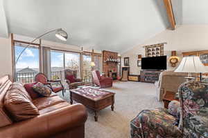 Living room with light carpet, vaulted ceiling with beams, and a fireplace