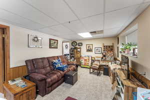 Carpeted living room featuring a paneled ceiling and wood walls