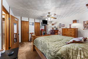 Carpeted bedroom featuring multiple closets, a textured ceiling, and ceiling fan