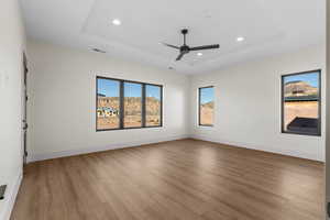 Empty room with ceiling fan, a tray ceiling, and light hardwood / wood-style floors