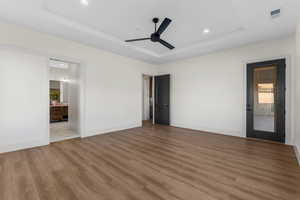 Unfurnished bedroom with ceiling fan, ensuite bathroom, hardwood / wood-style floors, and a tray ceiling