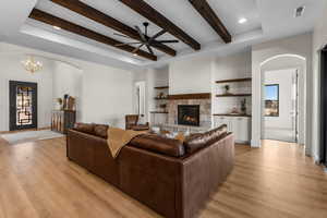 Living room with ceiling fan with notable chandelier, light hardwood / wood-style floors, built in features, and a stone fireplace