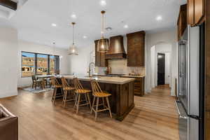 Kitchen featuring hanging light fixtures, an island with sink, custom range hood, high end fridge, and sink