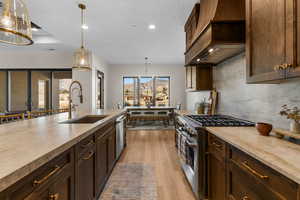 Kitchen with custom exhaust hood, pendant lighting, light hardwood / wood-style floors, appliances with stainless steel finishes, and sink