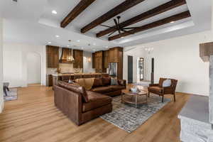 Living room featuring ceiling fan with notable chandelier, beamed ceiling, and light hardwood / wood-style flooring