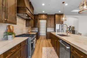 Kitchen with stainless steel appliances, sink, light wood-type flooring, custom exhaust hood, and pendant lighting