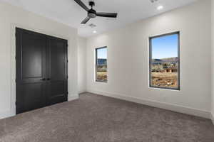 Unfurnished bedroom with ceiling fan, a closet, and dark colored carpet