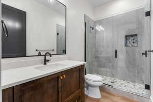 Bathroom featuring toilet, hardwood / wood-style flooring, a shower with door, and vanity