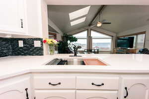 Kitchen featuring backsplash, vaulted ceiling, white cabinets, and ceiling fan