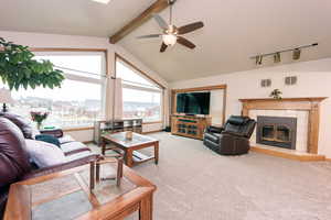 Living room with lofted ceiling with beams, ceiling fan, a fireplace, and carpet floors