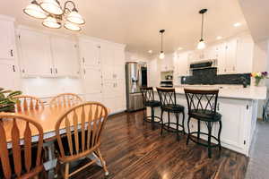 Kitchen with white cabinetry, range hood, and stainless steel refrigerator