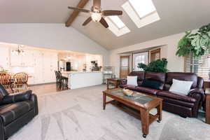 Living room with beam ceiling, ceiling fan with notable chandelier, high vaulted ceiling, and light colored carpet