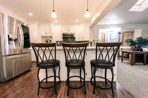 Kitchen with decorative light fixtures, stainless steel appliances, white cabinets, and a kitchen bar