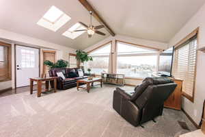 Carpeted living room with ceiling fan and vaulted ceiling with skylight