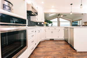 Kitchen featuring pendant lighting, tasteful backsplash, white cabinets, dark hardwood / wood-style flooring, and stainless steel appliances