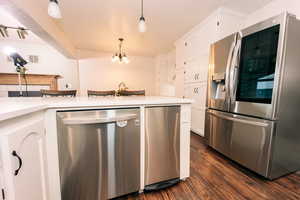 Kitchen featuring stainless steel appliances, white cabinetry, hanging light fixtures, and dark wood-type flooring