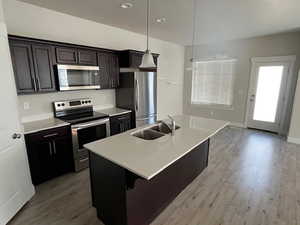 Kitchen featuring a kitchen island with sink, light wood-style floors, light countertops, and appliances with stainless steel finishes