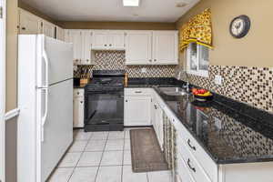 Kitchen with sink, white cabinets, dark stone counters, white refrigerator, and black gas stove