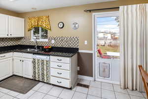 Kitchen featuring tasteful backsplash, dishwasher, sink, white cabinets, and light tile patterned floors