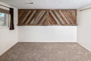 Carpeted empty room with a textured ceiling and wood walls