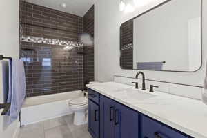 Full bathroom with vanity, tiled shower / bath combo, tile patterned floors, and toilet