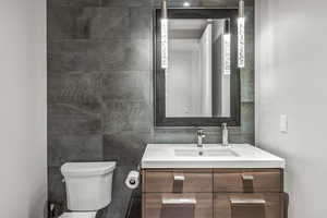 Bathroom featuring vanity, tile walls, and toilet