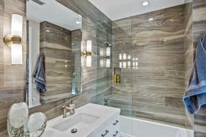 Bathroom with vanity, tiled shower / bath combo, and tile walls