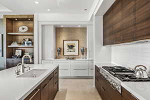 Kitchen with dark brown cabinetry, stainless steel gas cooktop, sink, white cabinetry, and light tile patterned floors