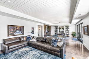 Living room with concrete flooring, a raised ceiling, and wooden ceiling