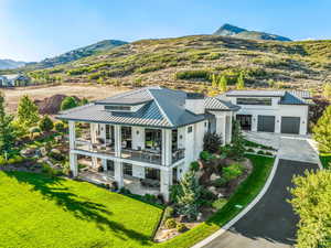 Back of property with a patio, a balcony, a lawn, a garage, and a mountain view