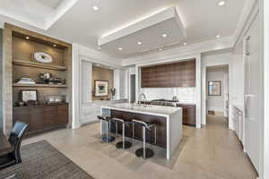 Kitchen featuring built in features, white cabinetry, an island with sink, sink, and a breakfast bar area