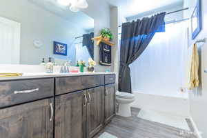 Full bathroom featuring hardwood / wood-style flooring, vanity, shower / bathtub combination with curtain, and toilet