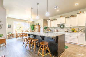 Kitchen with white cabinetry, decorative light fixtures, a kitchen island with sink, and light stone countertops