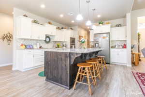 Kitchen with a kitchen bar, white cabinetry, a center island with sink, pendant lighting, and stainless steel appliances