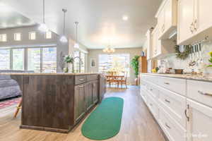 Kitchen featuring white cabinetry, hanging light fixtures, dark brown cabinetry, a center island with sink, and decorative backsplash