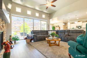 Living room with ceiling fan with notable chandelier, a stone fireplace, a towering ceiling, and hardwood / wood-style floors